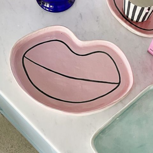 En rosa tallrik formad som läppar med svart kontur, placerad på ett marmorliknande bord.