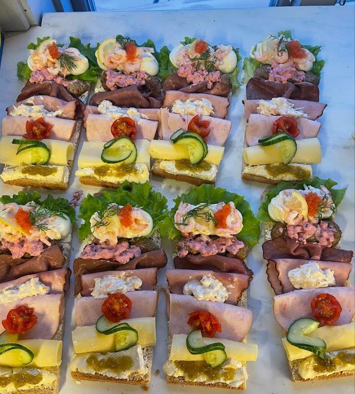 Ett fat med smörgåsar med olika pålägg som skinka, räkor, ost och grönsaker, dekorerade med sallad.