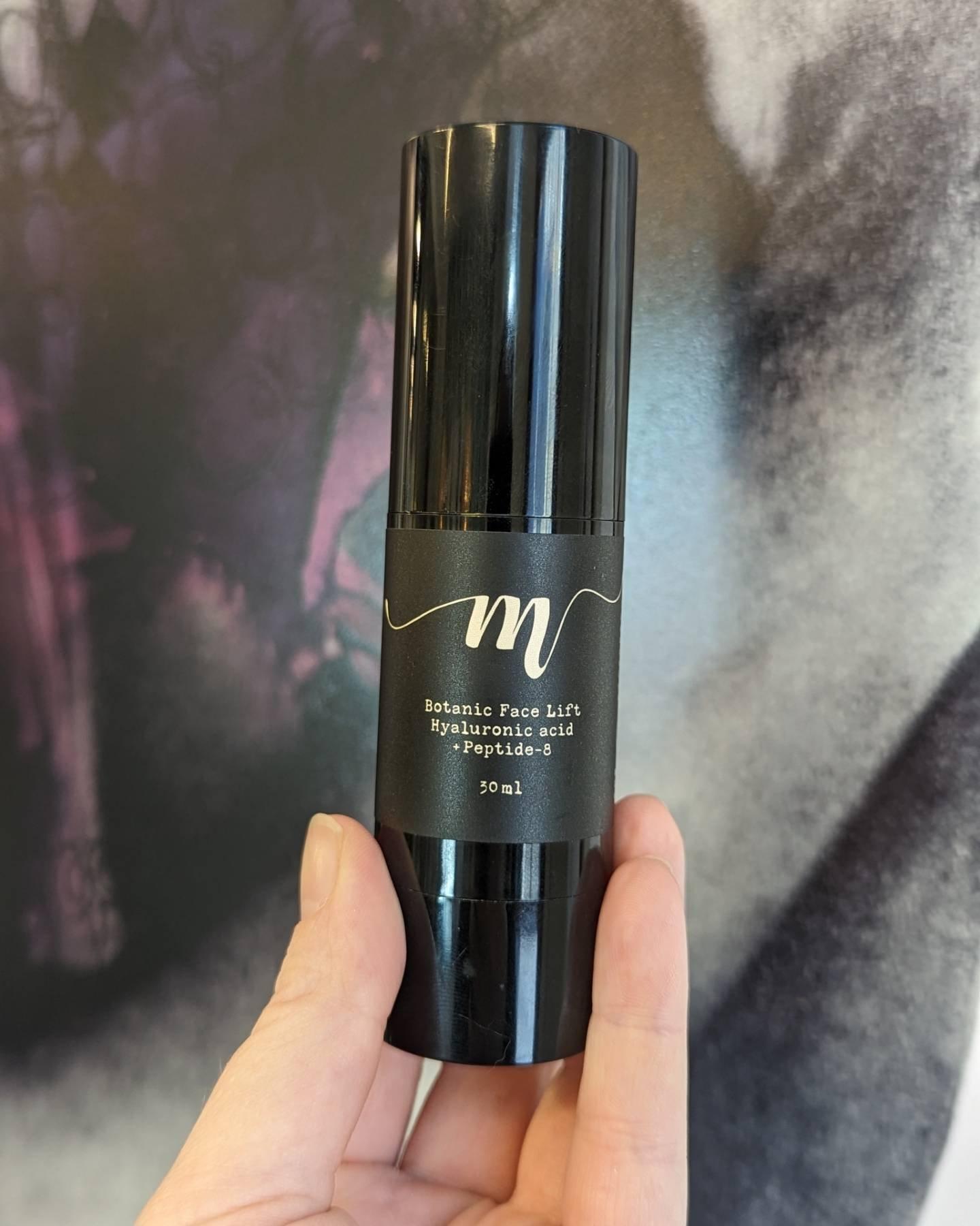 Svart ansiktskräm i en pumpflaska med etikett, hålls i hand, 30 ml.
