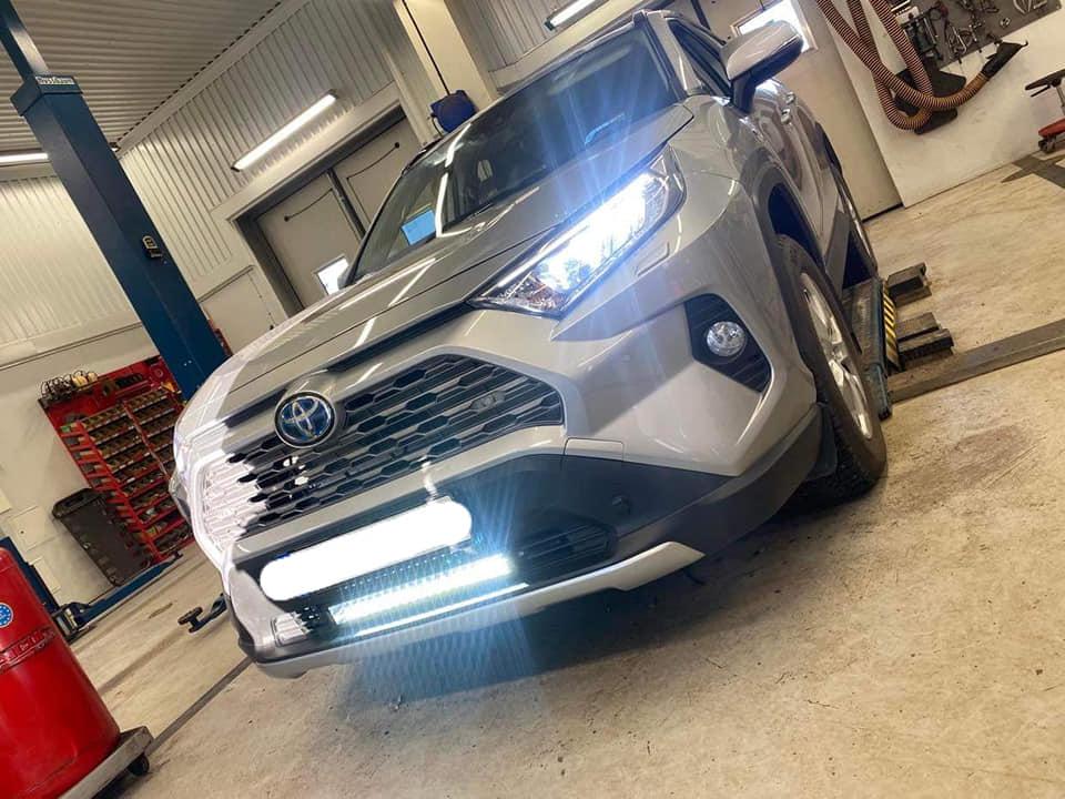En silverfärgad Toyota RAV4 står i en verkstad med verktyg och utrustning i bakgrunden.