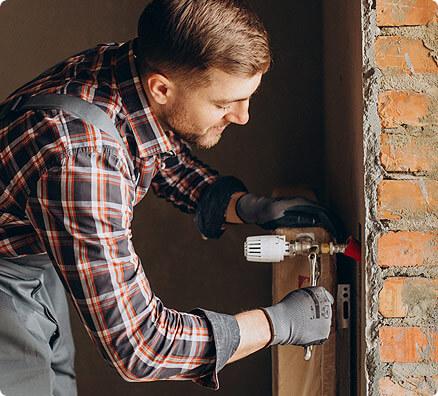 En hantverkare installerar en apparat med en skruvdragare i ett rum med tegelväggar.