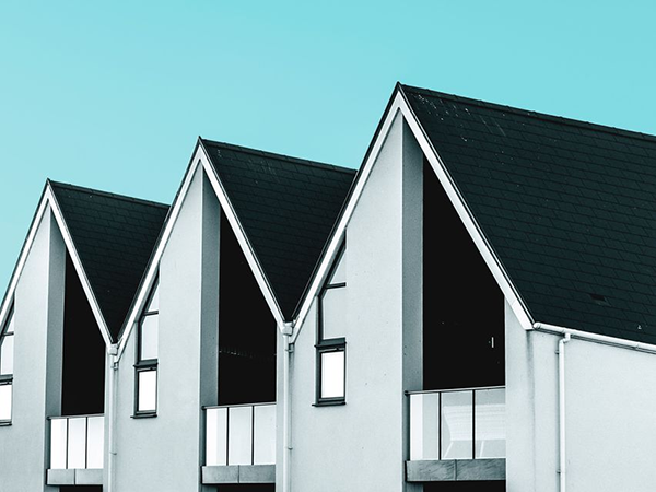 Flera moderna hus med svarta tak och balkonger mot en ljusblå himmel.