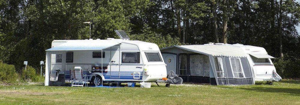 Två husvagnar parkerade på en grön campingplats omgiven av träd och gräs.