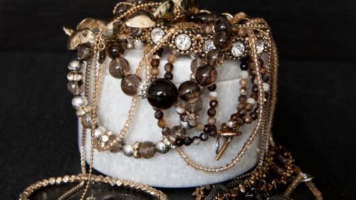 En vit smyckesask fylld med olika halsband och armband i bruna och gyllene nyanser.