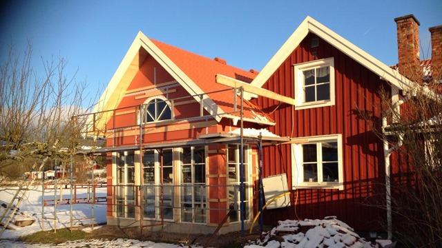 Ett rött hus med vit träpanel och tak av tegel, omgiven av snö och byggställningar.