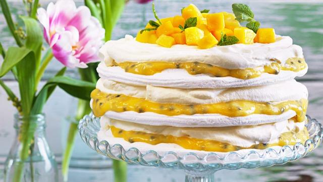 En hög med pavlova toppad med mango och passionsfrukt, omgiven av färska tulpaner i vaser.