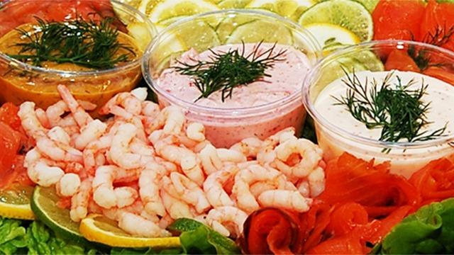Färska räkor med såser i skålar, omgiven av citroner, lime och lax på en grönsaksbädd.