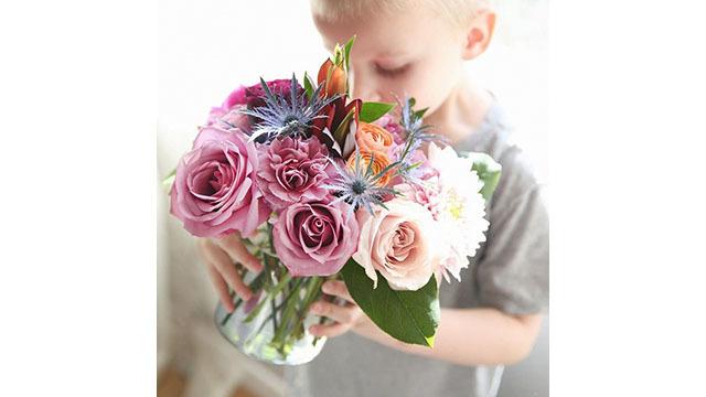 Ett barn håller en bukett med rosa och vita blommor, inklusive rosor och andra färgglada blommor.
