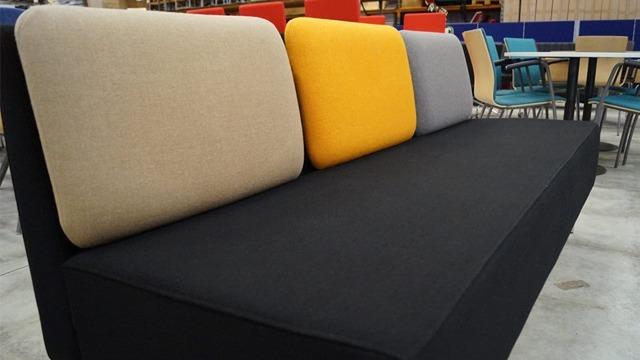 En modern soffa med svarta ben och kuddar i beige, gul och grå färg.