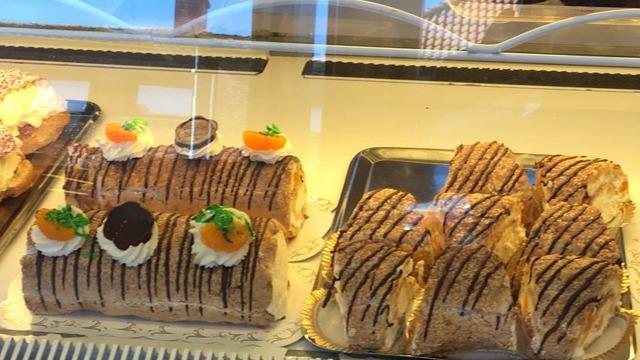 Flera bakverk i en glasskåp, inklusive rulltårtor med grädde, choklad och apelsinbitar.