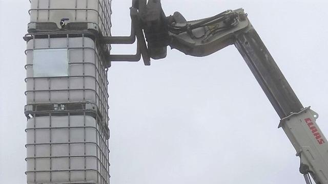 En grävmaskin som lyfter en stor behållare på en byggarbetsplats under en molnig himmel.