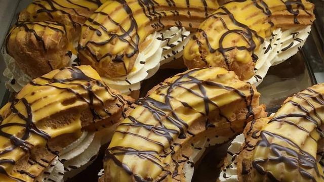 Flera stora bakverk med grädde och chokladglasyr i en glasskåp.