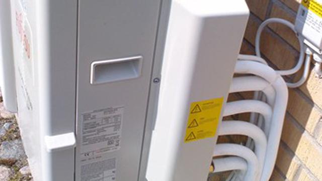 En värmepump installerad på en vägg med rör och varningsskyltar.