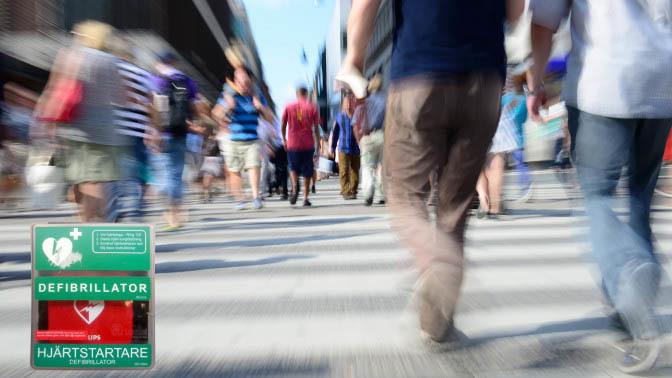 Människor som går över ett övergångsställe med en defibrillator och hjärtstartare i fokus.