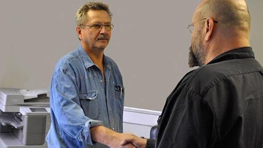 Två män skakar hand i ett kontorsutrymme, med en skrivare i bakgrunden.