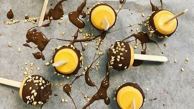 Flera chokladöverdragna glassar med nötter på en bakplåt, omgivna av smält choklad.