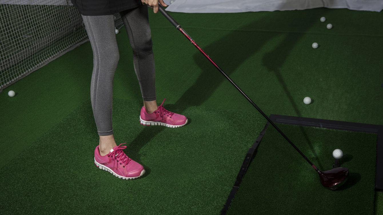 En person i rosa skor står på en golfträning med golfbollar på gräset.