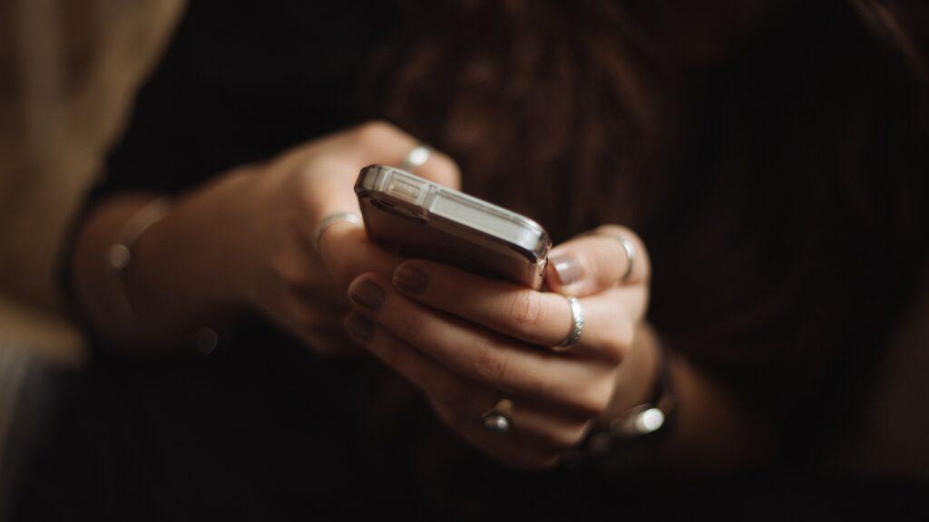 En person som håller en smartphone i händerna, med fokus på ringar på fingrarna.