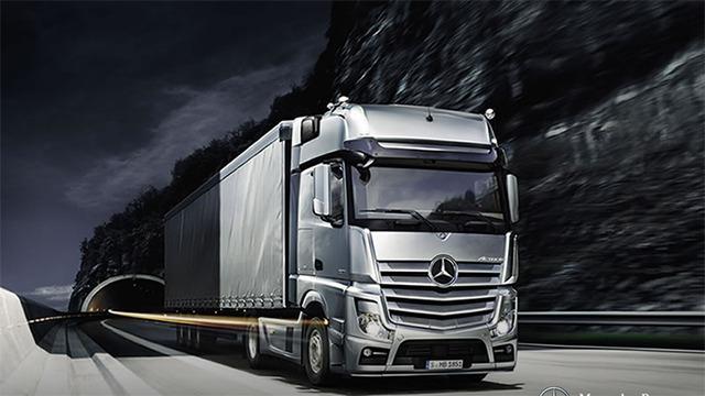 En silverfärgad lastbil från Mercedes kör på en väg nära en tunnel i en mörk landskap.