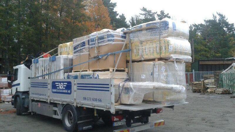 Lastbil med högar av paket och byggmaterial, lastad och redo för transport.