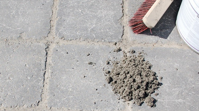En hög med cement på en stenlagd yta med en borste och en burk i bakgrunden.