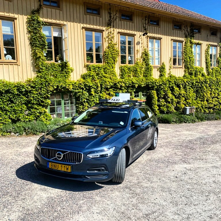 En svart Volvo bil parkerad framför en träbyggnad täckt av gröna växter.
