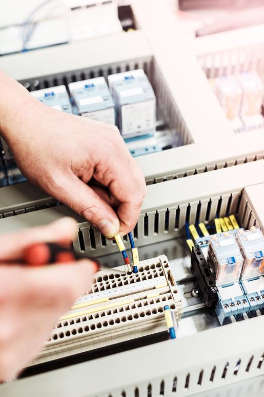 En person kopplar kablar i en elektrisk låda med reläer och anslutningar.