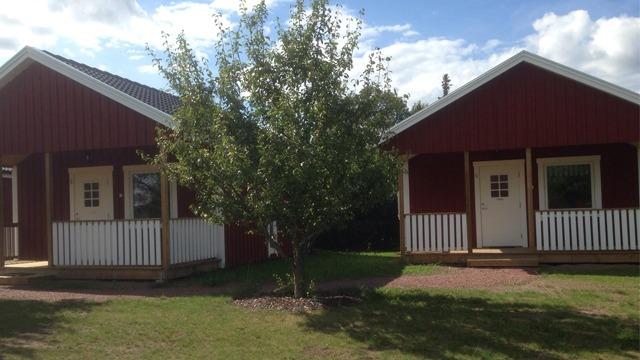 Två röda stugor med vita detaljer, omgivna av grön gräsmatta och en liten trädgård.