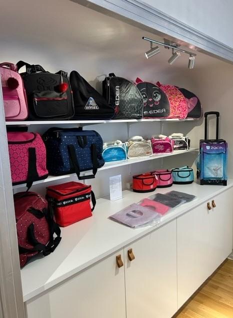 Flera färgglada väskor och sportbagar på en hylla i en butik, inklusive ryggsäckar och handväskor.