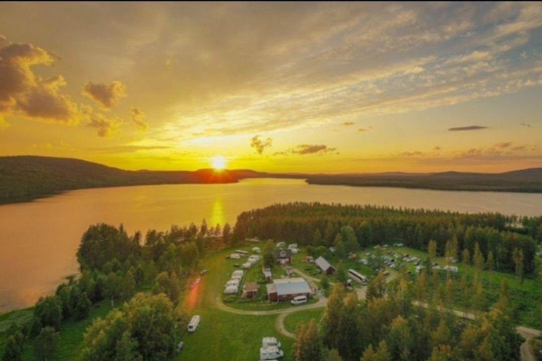 En solnedgång över en sjö med campingplatser och grönskande träd i fjärran.